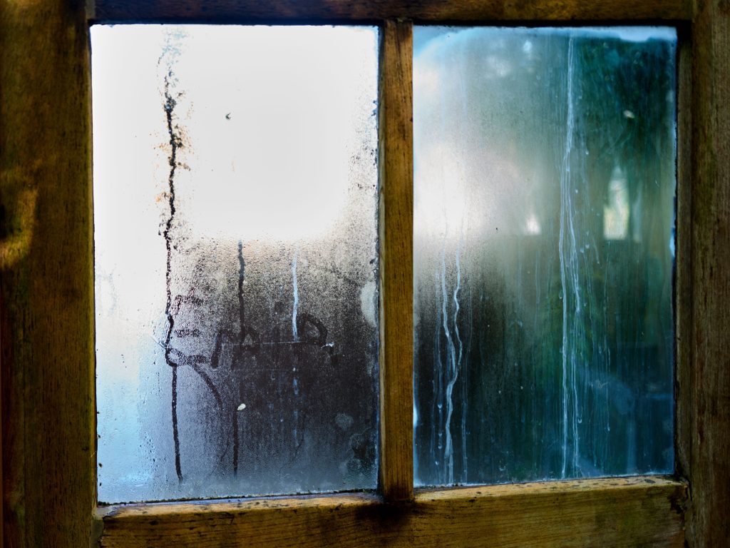 Beschlagene Fensterscheibe mit Kondenswasser am Holzrahmen
