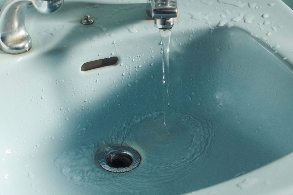 Wasser läuft aus dem Wasserhahn in den Abfluss eines Waschbeckens