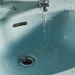 Wasser läuft aus dem Wasserhahn in den Abfluss eines Waschbeckens
