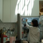 Person im Schlafanzug steht vor dem geöffneten Kühlschrank in der Küche