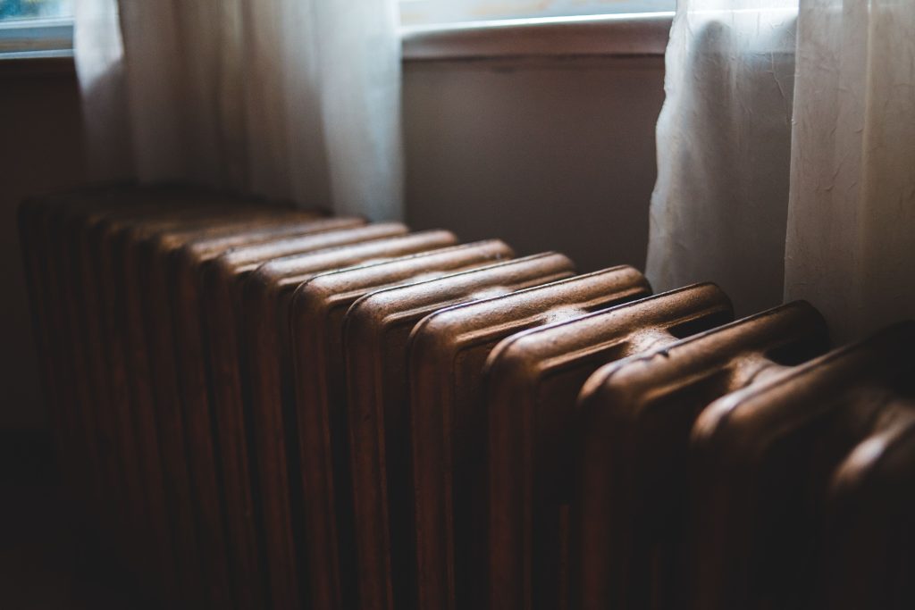 Alter Gussheizkörper unter einem Fenster mit Vorhang im Wohnraum