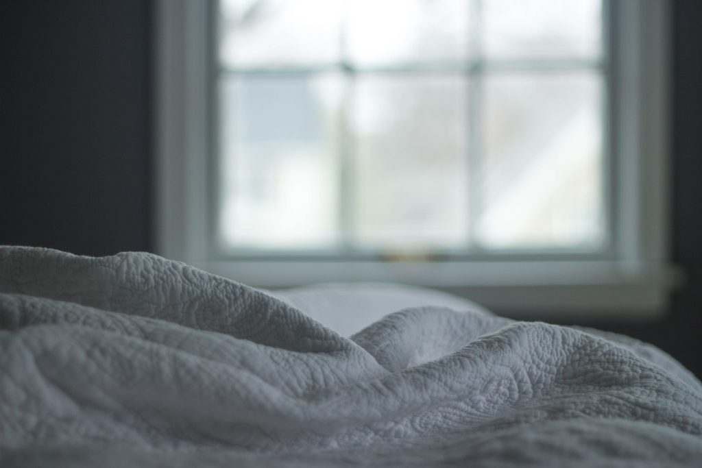 Zerknittertes Bett vor einem Fenster im Schlafzimmer im kühlen Morgenlicht