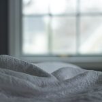 Zerknittertes Bett vor einem Fenster im Schlafzimmer im kühlen Morgenlicht