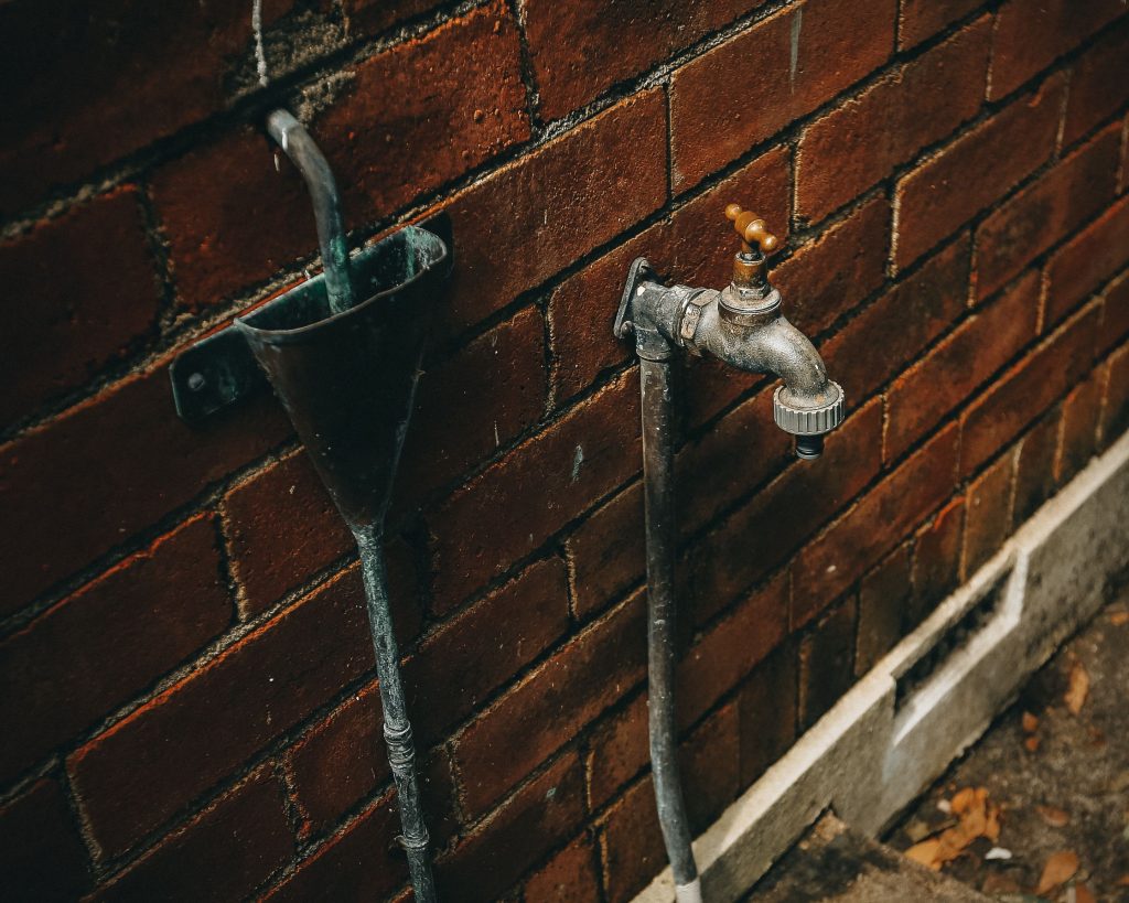 Alter Außenwasserhahn an einer verwitterten Backsteinwand