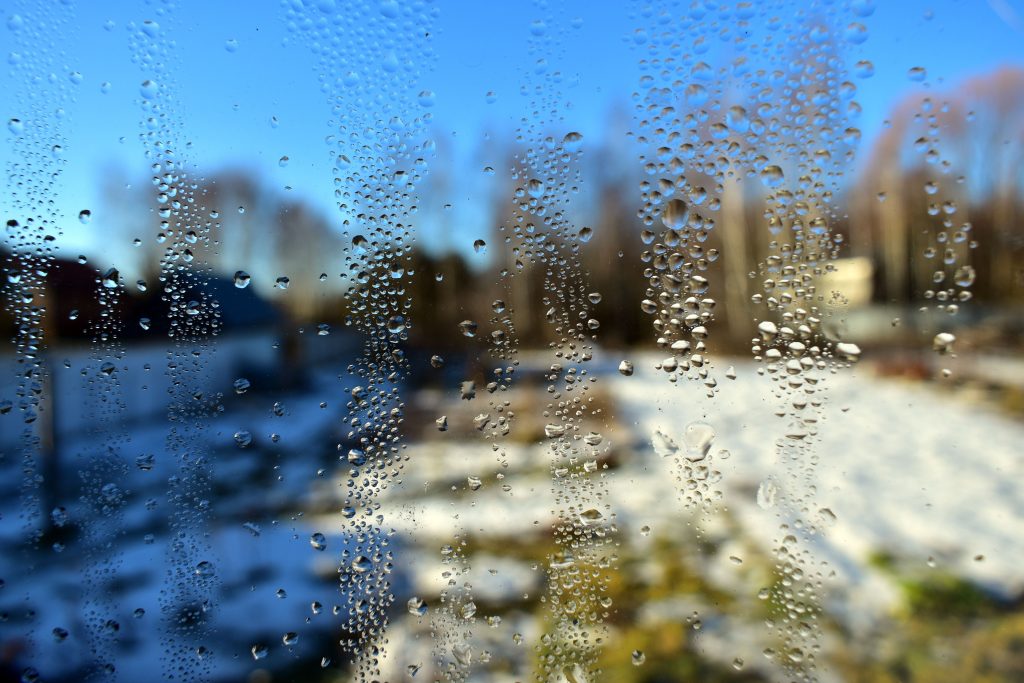 Fenster mit Wassertropfen und Blick auf eine verschneite Winterlandschaft
