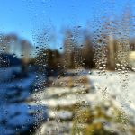 Fenster mit Wassertropfen und Blick auf eine verschneite Winterlandschaft