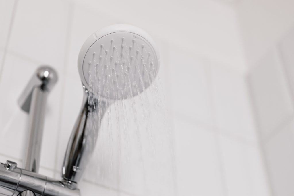 Duschkopf mit Wasserstrahl in einem weiß gefliesten Bad