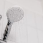 Duschkopf mit Wasserstrahl in einem weiß gefliesten Bad